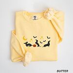 Butter crewneck sweatshirt laid flat on white, embroidered with three black and tan dachshunds playing under a yellow crescent moon, gold stars and flying bats beside a small jack-o'-lantern