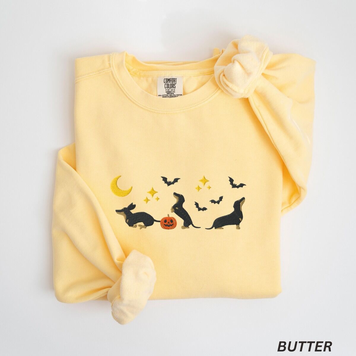 Black and Tan Dachshund Halloween Sweatshirt – Butter Butter crewneck sweatshirt laid flat on white, embroidered with three black and tan dachshunds playing under a yellow crescent moon, gold stars and flying bats beside a small jack-o'-lantern