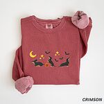 Crimson crewneck sweatshirt laid flat on white, embroidered with three black and tan dachshunds playing under a yellow crescent moon, gold stars and flying bats beside a small jack-o'-lantern