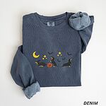 Denim crewneck sweatshirt laid flat on white, embroidered with three black and tan dachshunds playing under a yellow crescent moon, gold stars and flying bats beside a small jack-o'-lantern