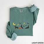 Light Green crewneck sweatshirt laid flat on white, embroidered with three black and tan dachshunds playing under a yellow crescent moon, gold stars and flying bats beside a small jack-o'-lantern