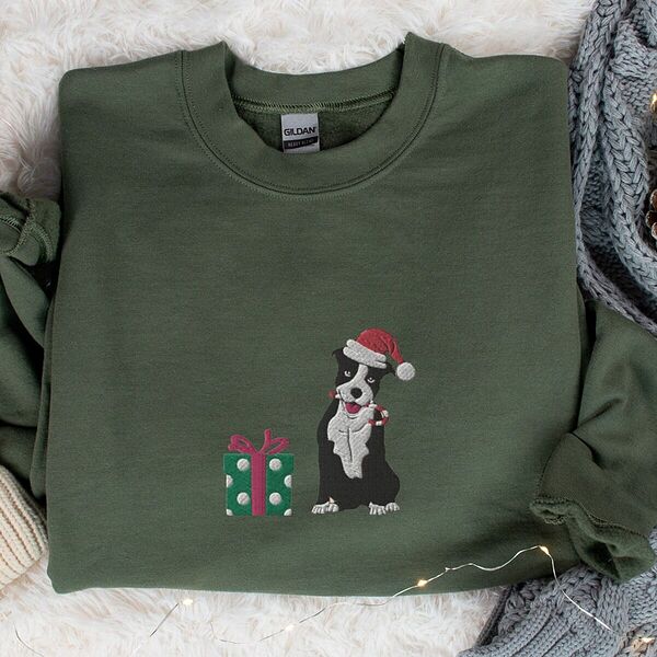 Military Green crewneck sweatshirt laid flat on a faux fur rug with a knit blanket, embroidered with a black and white pitbull in a Santa hat holding a candy cane beside a green polka dot gift box