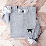 Sport Grey crewneck sweatshirt laid flat on a wood floor, embroidered with a small minimalist black and white pit bull face with a white blaze and grey ears on the left chest