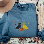 Indigo Blue crewneck sweatshirt laid flat with a hat and pampas grass, embroidered with a black Labrador and a yellow Labrador sitting by three pumpkins under falling autumn leaves