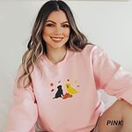 Smiling woman in a Light Pink crewneck sweatshirt embroidered with a black Labrador and a yellow Labrador sitting by three pumpkins under falling autumn leaves