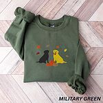 Military Green crewneck sweatshirt laid flat on herringbone wood, embroidered with a black Labrador and a yellow Labrador sitting by three pumpkins under falling autumn leaves