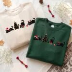 Two black cat Christmas sweatshirts in cream and forest green with the same embroidered holiday cats