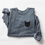 Dark Heather crewneck sweatshirt laid flat with rolled sleeves, embroidered with a solid black cat face with yellow eyes on the left chest