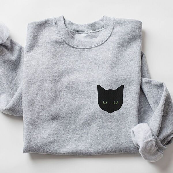 Sport Grey crewneck sweatshirt laid flat with a rolled sleeve, embroidered with a solid black cat face with green eyes on the left chest
