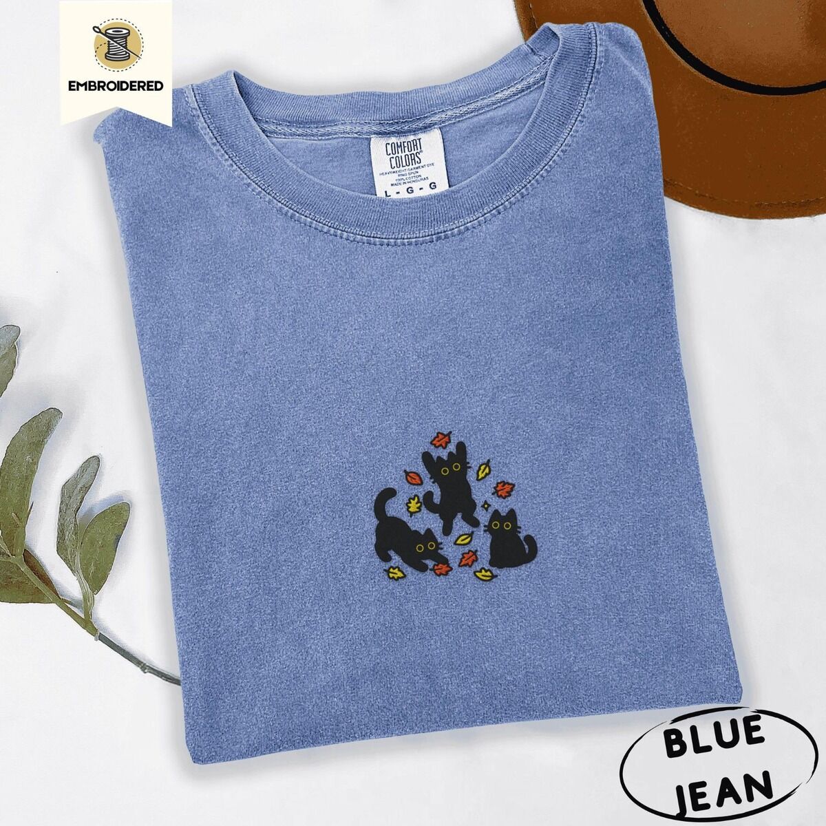 Black Cat Fall Shirt – Blue Jean Blue Jean Comfort Colors T-shirt embroidered with three black cats pouncing, leaping and sitting among falling red, orange and yellow autumn leaves