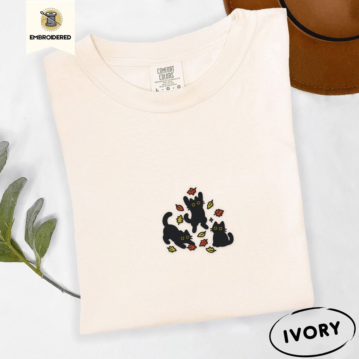 Black Cat Fall Shirt – Ivory Ivory Comfort Colors T-shirt embroidered with three black cats pouncing, leaping and sitting among falling red, orange and yellow autumn leaves