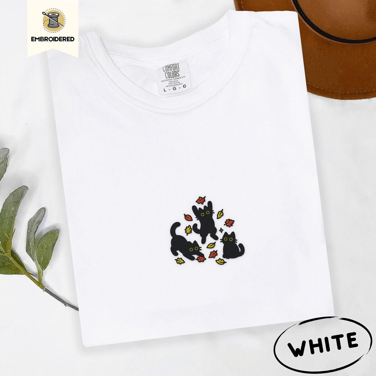 Black Cat Fall Shirt – White White Comfort Colors T-shirt embroidered with three black cats pouncing, leaping and sitting among falling red, orange and yellow autumn leaves
