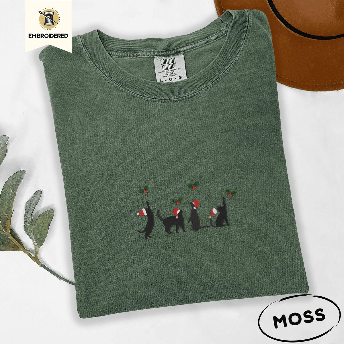 Black Cat Santa Hat Shirt – Moss Moss Comfort Colors T-shirt embroidered with four black cat silhouettes in Santa hats reaching for holly across the chest