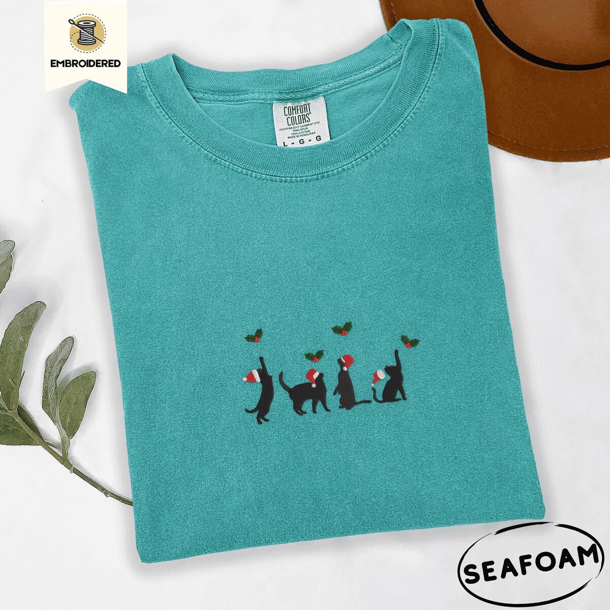 Black Cat Santa Hat Shirt – Seafoam Seafoam Comfort Colors T-shirt embroidered with four black cat silhouettes in Santa hats reaching for holly across the chest