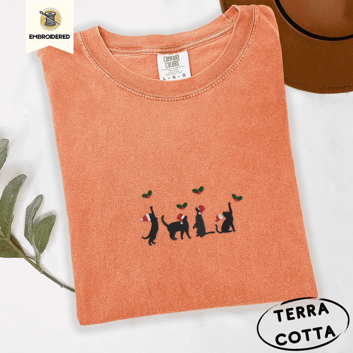 Black Cat Santa Hat Shirt – Terracotta Terracotta Comfort Colors T-shirt embroidered with four black cat silhouettes in Santa hats reaching for holly across the chest