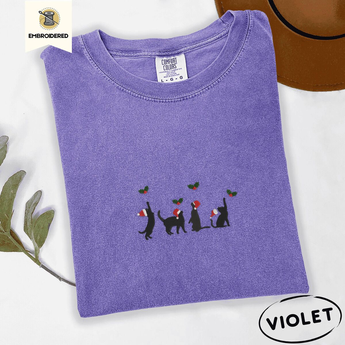 Black Cat Santa Hat Shirt – Violet Violet Comfort Colors T-shirt embroidered with four black cat silhouettes in Santa hats reaching for holly across the chest