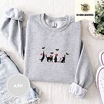 Ash crewneck sweatshirt folded with denim shorts, white sneakers and a potted plant, embroidered with four black cat silhouettes in Santa hats reaching for holly across the chest