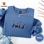 Indigo Blue crewneck sweatshirt folded with light jeans and dried twigs, embroidered with four black cat silhouettes in Santa hats reaching for holly across the chest