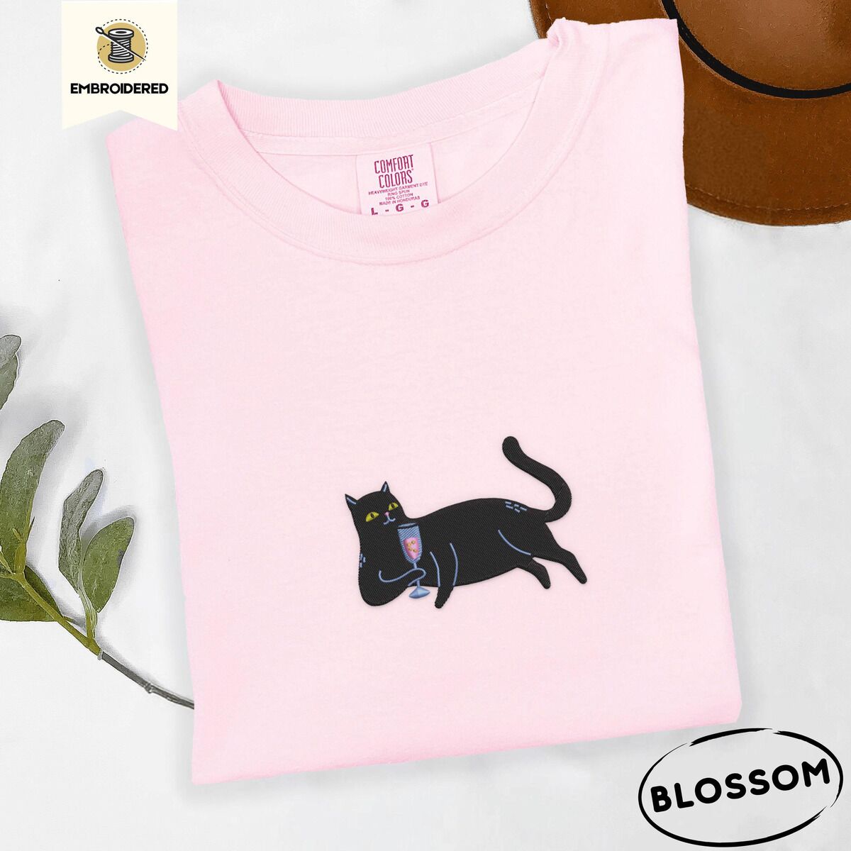 Black Cat Wine Shirt – Blossom Blossom Comfort Colors T-shirt embroidered with a black cat lounging on its side holding a stemmed glass of pink wine