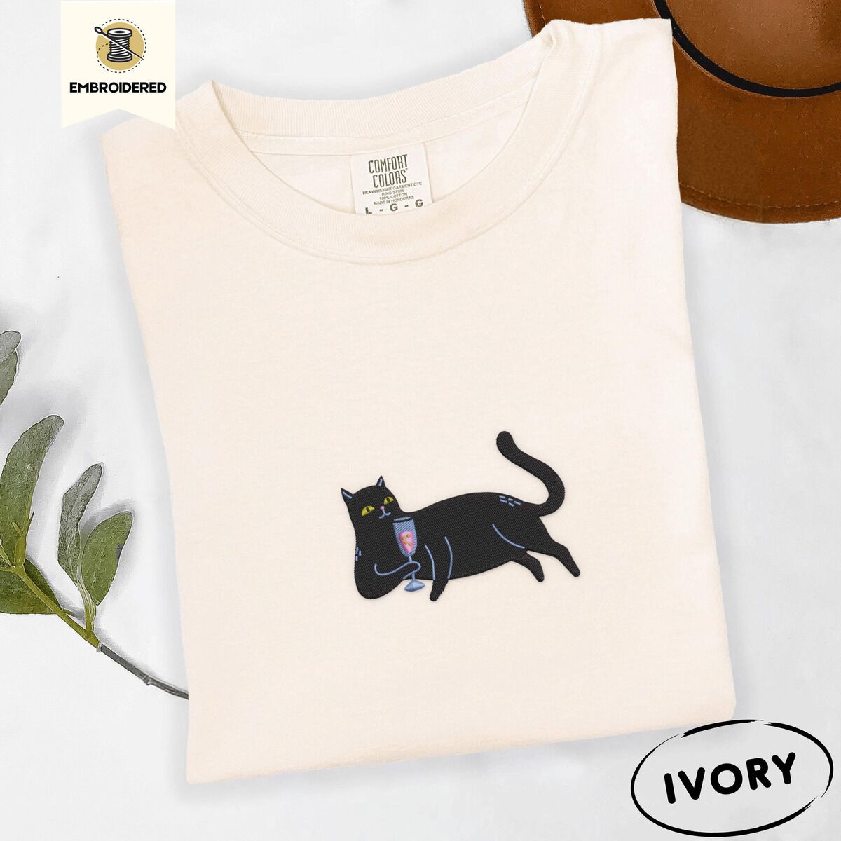 Black Cat Wine Shirt – Ivory Ivory Comfort Colors T-shirt embroidered with a black cat lounging on its side holding a stemmed glass of pink wine