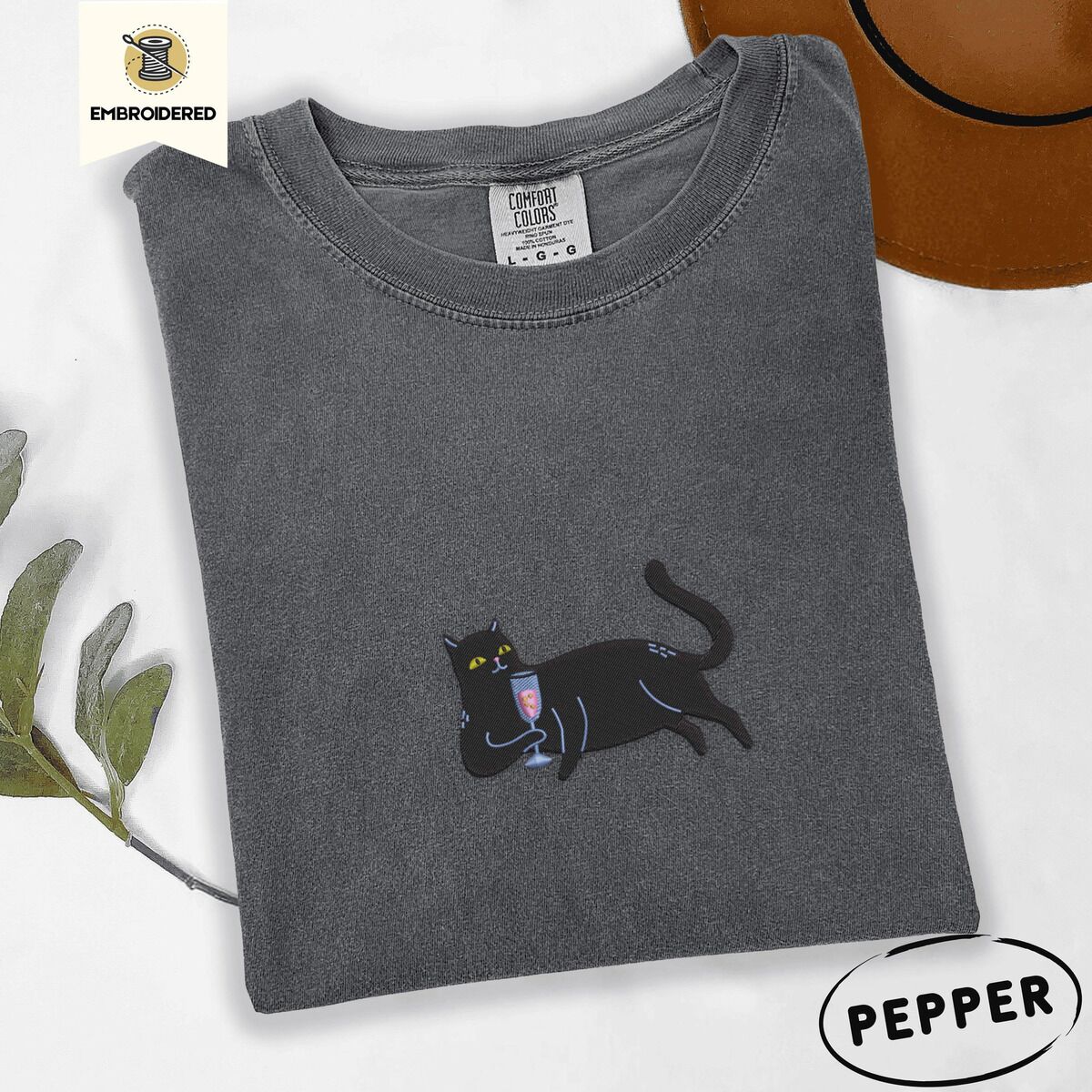 Black Cat Wine Shirt – Pepper Pepper Comfort Colors T-shirt embroidered with a black cat lounging on its side holding a stemmed glass of pink wine