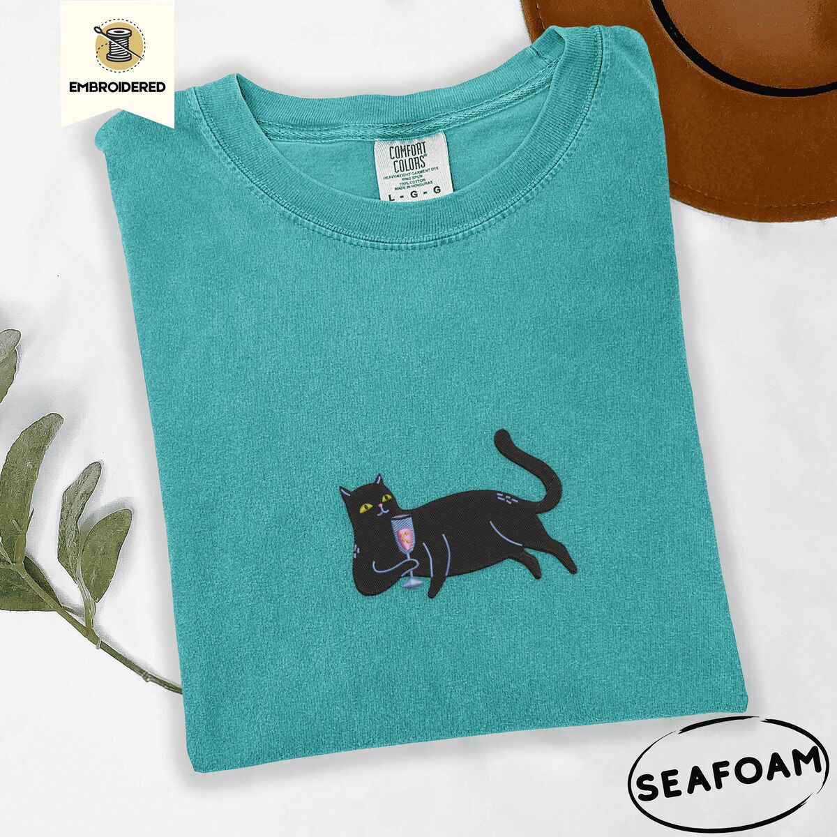 Black Cat Wine Shirt – Seafoam Seafoam Comfort Colors T-shirt embroidered with a black cat lounging on its side holding a stemmed glass of pink wine