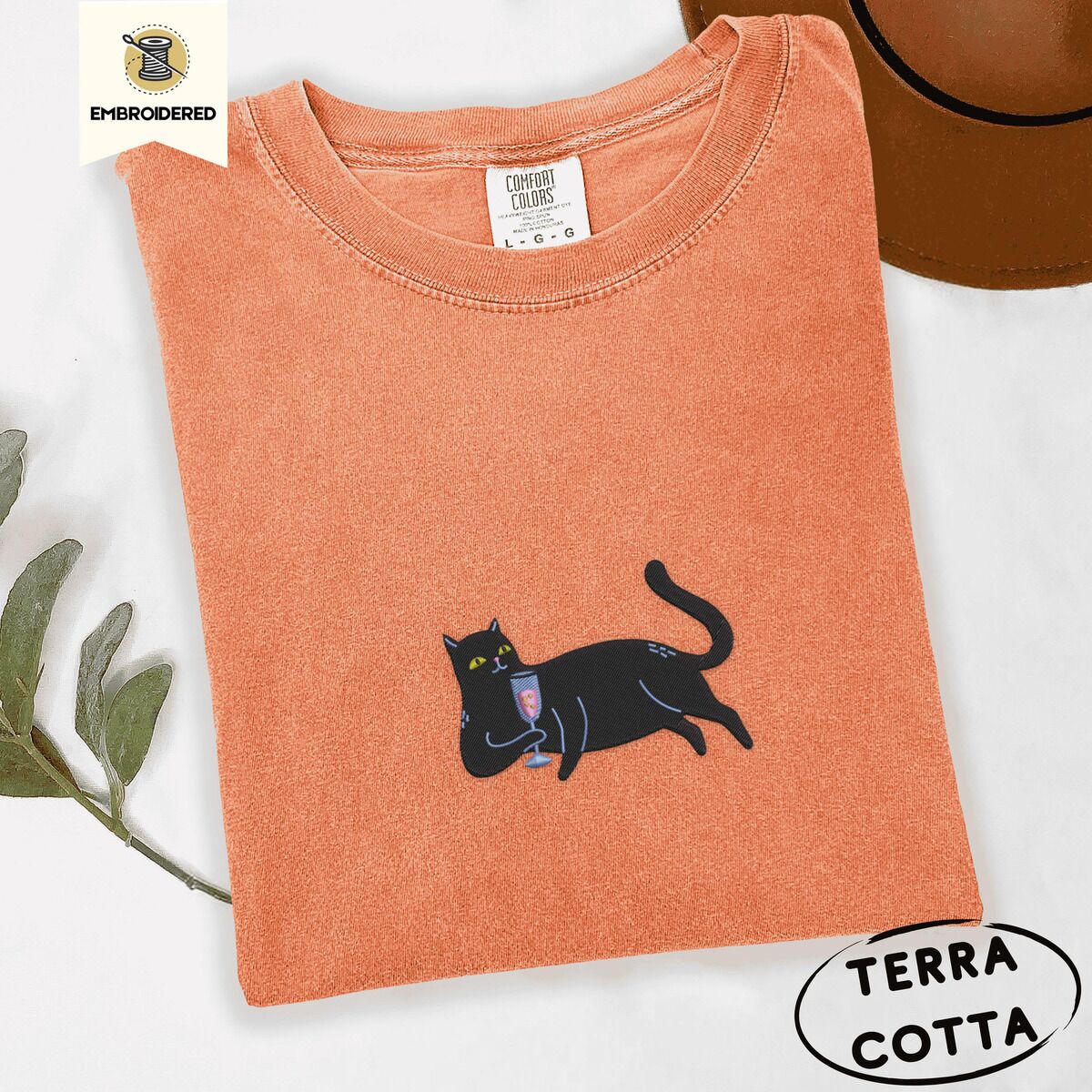 Black Cat Wine Shirt – Terracotta Terracotta Comfort Colors T-shirt embroidered with a black cat lounging on its side holding a stemmed glass of pink wine