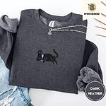 Dark Heather crewneck sweatshirt folded with ripped jeans and a silver chain necklace, embroidered with a black cat lounging with a glass of pink wine in the center of the chest