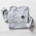 Sport Grey crewneck sweatshirt laid flat on a white background, embroidered with a black cartoon doodle face with a pale grey outline and a pink tongue on the left chest