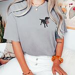 Woman sitting in a Grey T-shirt with a black lab silhouette carrying an American flag on the left chest