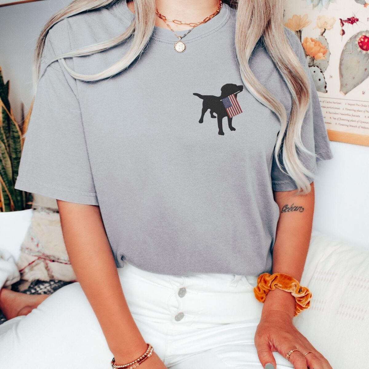 Black Lab American Flag Shirt - Grey Woman sitting in a Grey T-shirt with a black lab silhouette carrying an American flag on the left chest