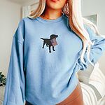 Woman in a Light Blue crewneck sweatshirt with a black lab holding a USA flag centered on the chest