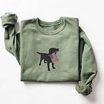 Military Green crewneck sweatshirt laid flat, a black Labrador holding a stars-and-stripes flag stitched across the chest