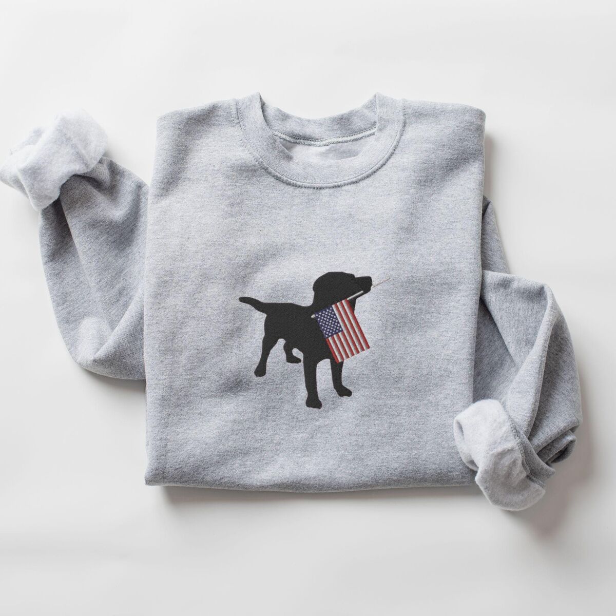 Black Lab American Flag Sweatshirt - Sport Grey Sport Grey crewneck sweatshirt laid flat with rolled sleeves, a black lab silhouette with an American flag stitched in the center