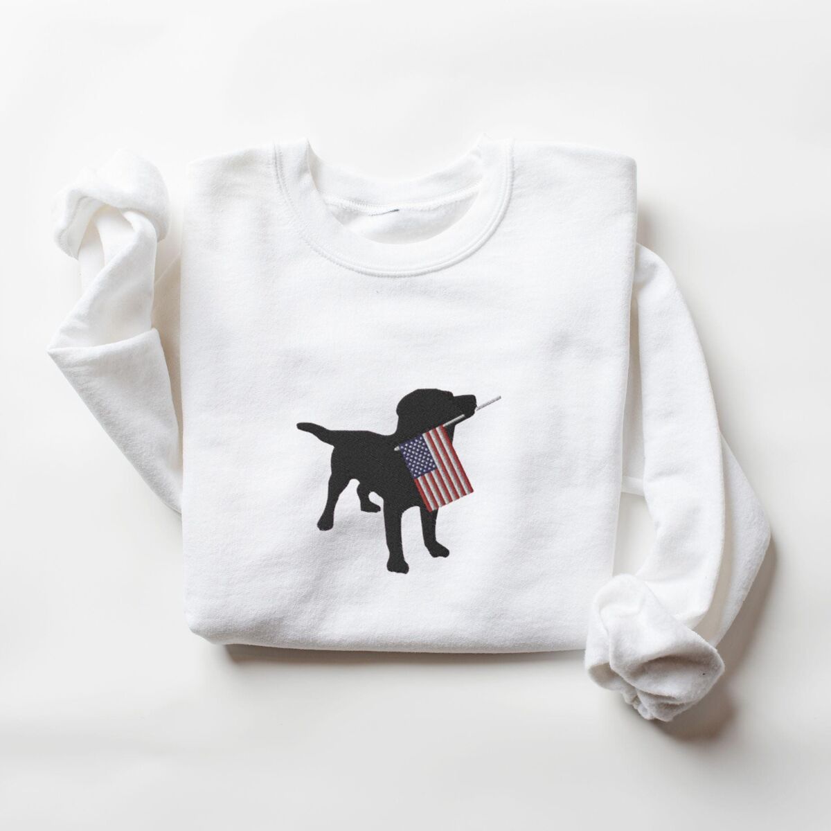 Black Lab American Flag Sweatshirt - White White crewneck sweatshirt laid flat, embroidered with a black Labrador carrying a red, white and blue flag