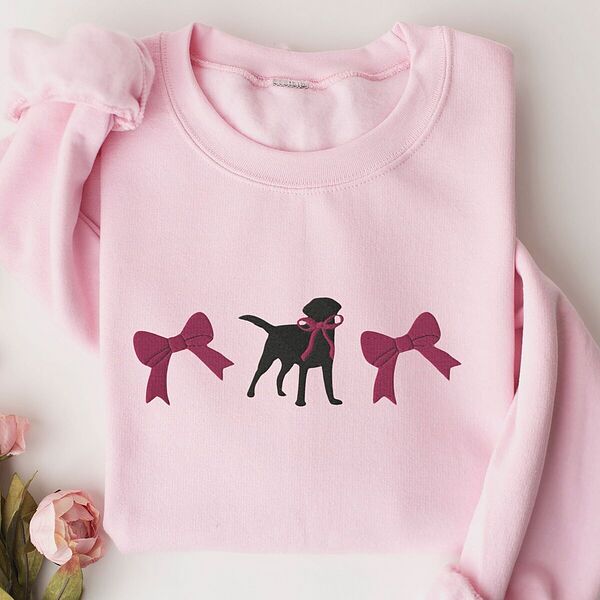 Light Pink crewneck sweatshirt laid flat with pink roses, embroidered with a black Labrador silhouette with a ribbon bow at its neck between two large raspberry pink bows across the chest