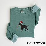 Light Green crewneck sweatshirt laid flat with rolled cuffs, embroidered with a black Labrador in a Santa hat carrying a string of Christmas lights