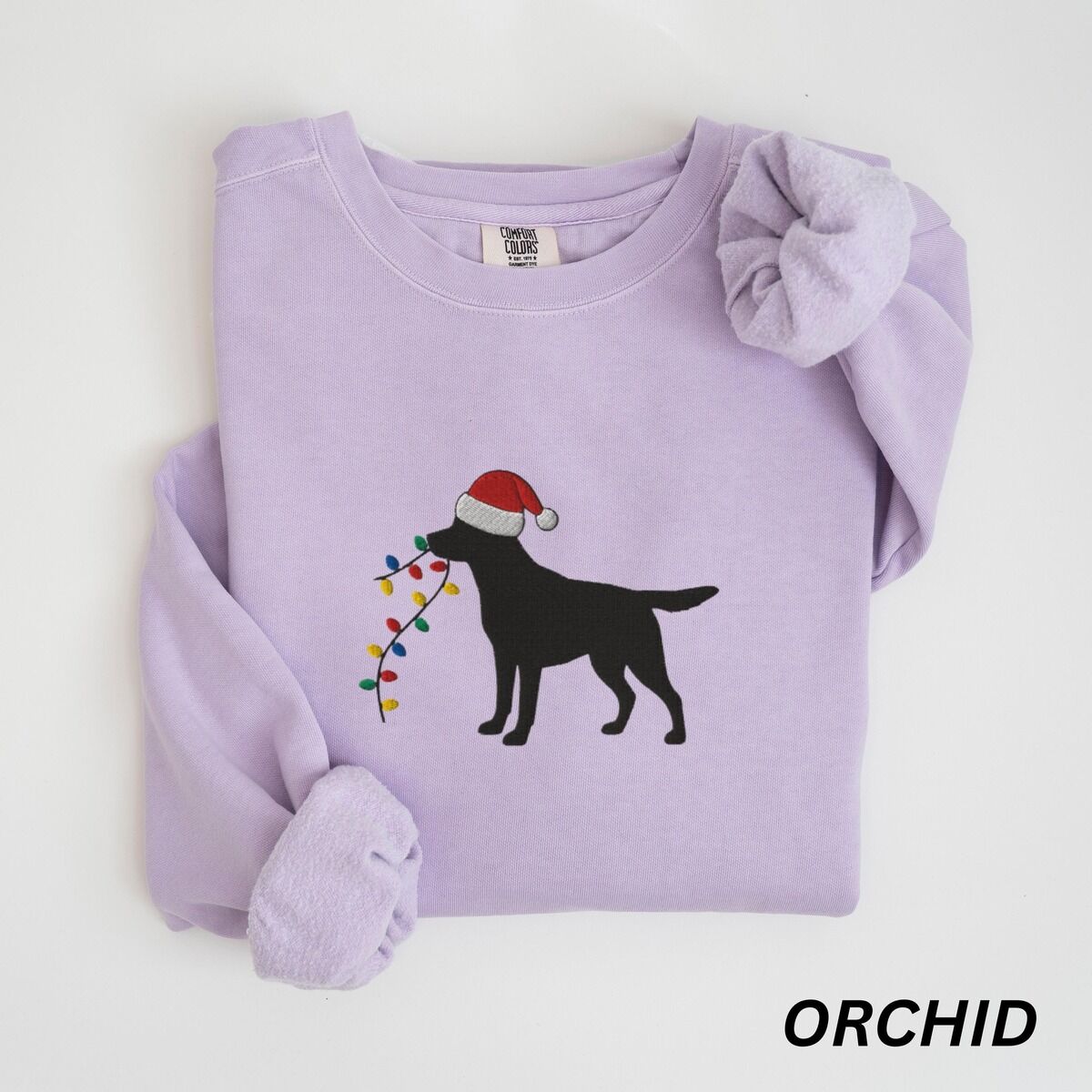 Black Lab Christmas Lights Sweatshirt – Orchid Orchid crewneck sweatshirt laid flat with rolled cuffs, embroidered with a black Labrador in a Santa hat carrying a string of Christmas lights