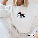 Woman sitting in a White crewneck sweatshirt embroidered with a black Labrador in a Santa hat carrying a string of Christmas lights