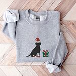Sport Grey crewneck sweatshirt laid flat on a chevron wood floor, embroidered with a sitting black Labrador in a Santa hat and red booties beside a green gift box
