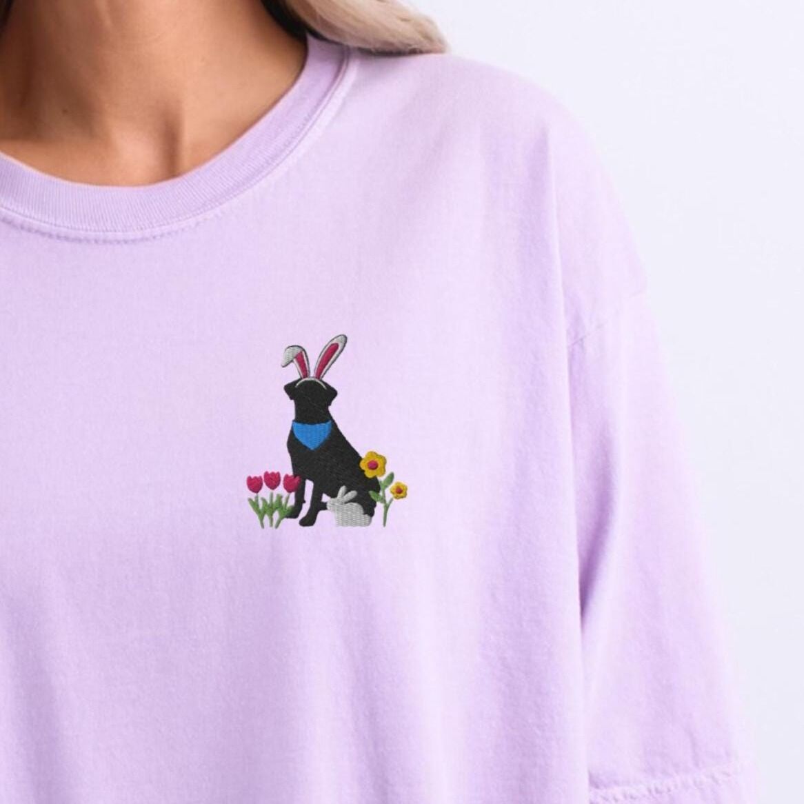 Black Lab Easter Shirt - Orchid Woman wearing a Orchid T-shirt embroidered with a sitting black lab in bunny ears and a blue bandana with pink tulips, yellow flowers and a little bunny on the left chest