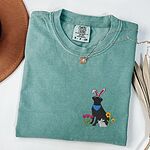 Seafoam T-shirt folded with a gold necklace, embroidered with a sitting black lab in bunny ears and a blue bandana with pink tulips, yellow flowers and a little bunny on the left chest