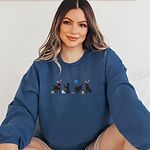 Smiling woman in a Indigo Blue crewneck sweatshirt embroidered with four black lab silhouettes in bunny ears with a little bunny, Easter eggs, daffodils and a blue balloon