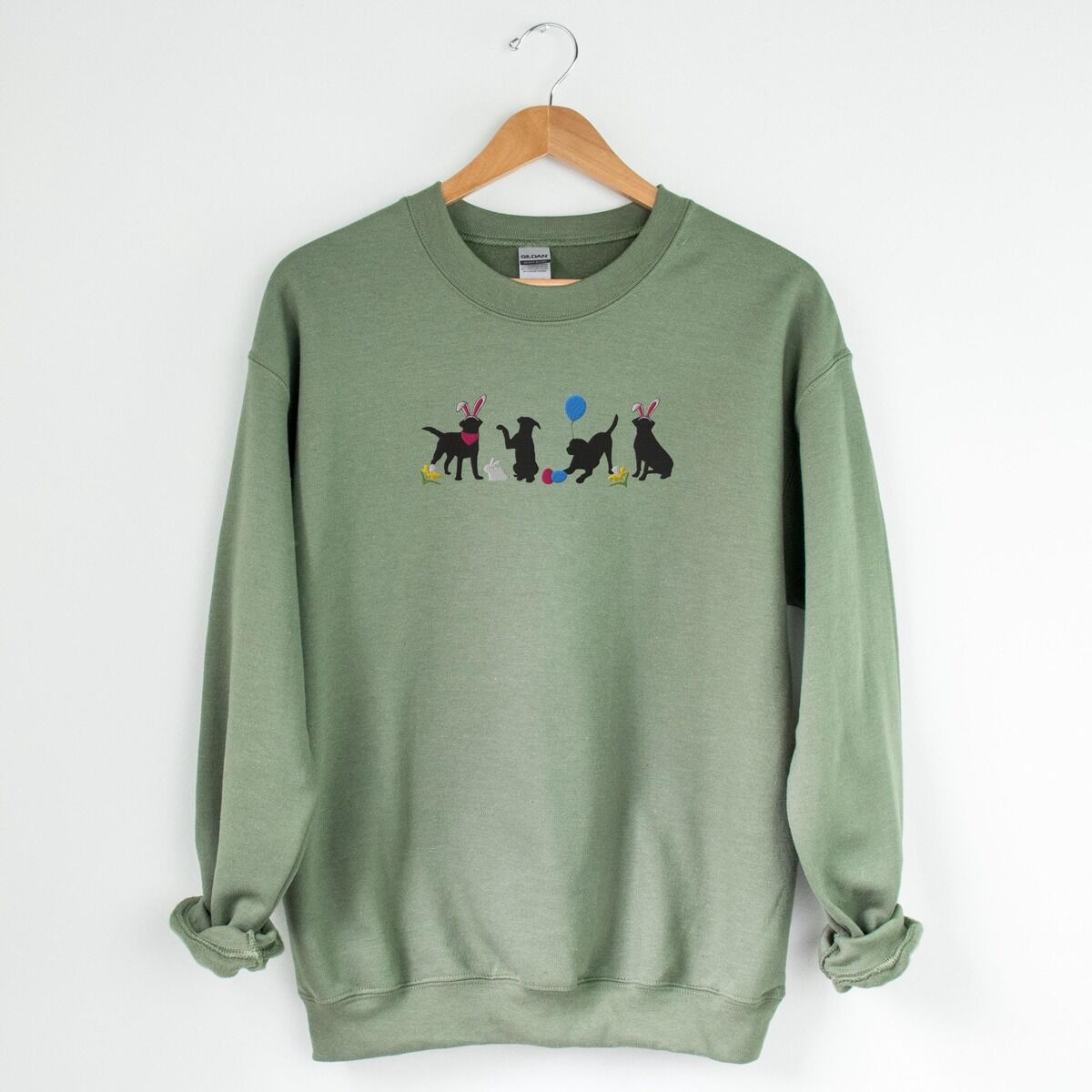 Black Lab Easter Sweatshirt – Military Green Military Green crewneck sweatshirt on a hanger, embroidered with four black lab silhouettes in bunny ears with a little bunny, Easter eggs, daffodils and a blue balloon