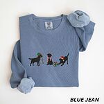 Blue Jean crewneck sweatshirt laid flat with rolled cuffs, embroidered with three black Labradors, one in an elf hat carrying Christmas lights, one in a candy-cane scarf and one in a Santa hat pawing a gift