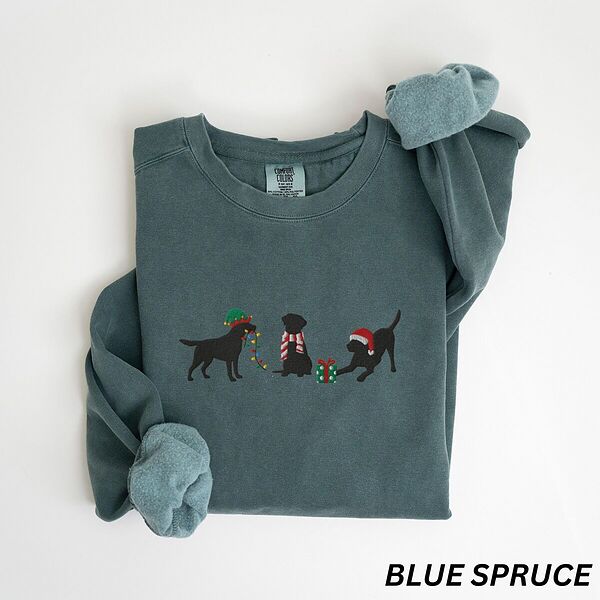 Blue Spruce crewneck sweatshirt laid flat with rolled cuffs, embroidered with three black Labradors, one in an elf hat carrying Christmas lights, one in a candy-cane scarf and one in a Santa hat pawing a gift