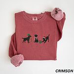 Crimson crewneck sweatshirt laid flat with rolled cuffs, embroidered with three black Labradors, one in an elf hat carrying Christmas lights, one in a candy-cane scarf and one in a Santa hat pawing a gift