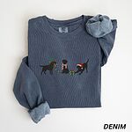 Denim crewneck sweatshirt laid flat with rolled cuffs, embroidered with three black Labradors, one in an elf hat carrying Christmas lights, one in a candy-cane scarf and one in a Santa hat pawing a gift