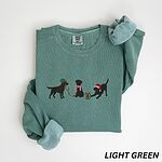 Light Green crewneck sweatshirt laid flat with rolled cuffs, embroidered with three black Labradors, one in an elf hat carrying Christmas lights, one in a candy-cane scarf and one in a Santa hat pawing a gift