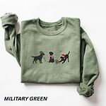 Military Green crewneck sweatshirt laid flat with a rolled cuff, embroidered with three black Labradors, one in an elf hat carrying Christmas lights, one in a candy-cane scarf and one in a Santa hat pawing a gift